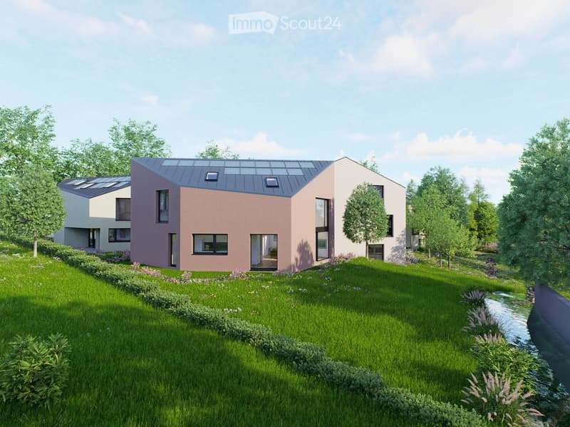 Modern two-story house with a combination of pink and white exterior walls, large windows, and a flat roof with skylights. The house is surrounded by a well-maintained lawn, shrubs, and trees, with a small water feature running alongside.