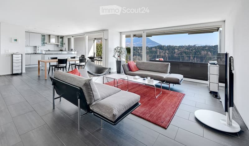Modern living room with grey sofa, coffee table, dining area, large windows offering a scenic mountain view, and contemporary furniture.