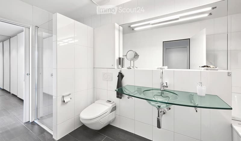 Modern bathroom with white tiles, a glass sink, a toilet, a large mirror, and a vanity cabinet.