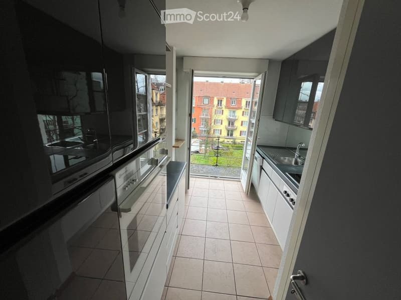 Modern kitchen with white and black cabinets, tiled floor, and a view of a cityscape through a large window. Includes a sink, faucet, oven, and dishwasher.