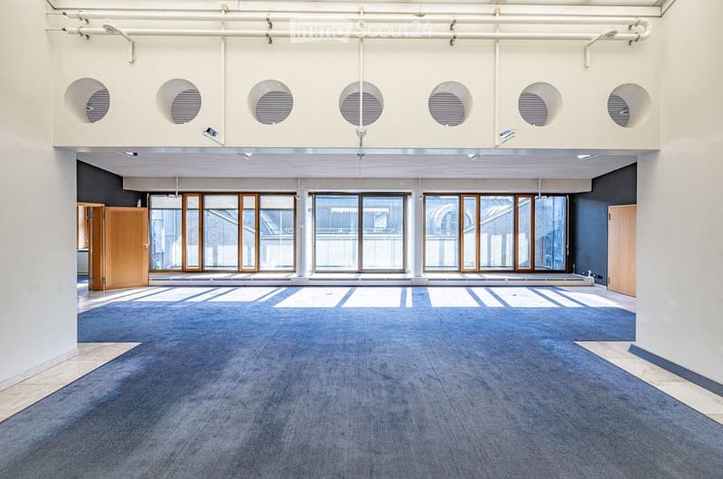 Empty room with blue carpet, large windows, and white walls. No furniture or equipment present.