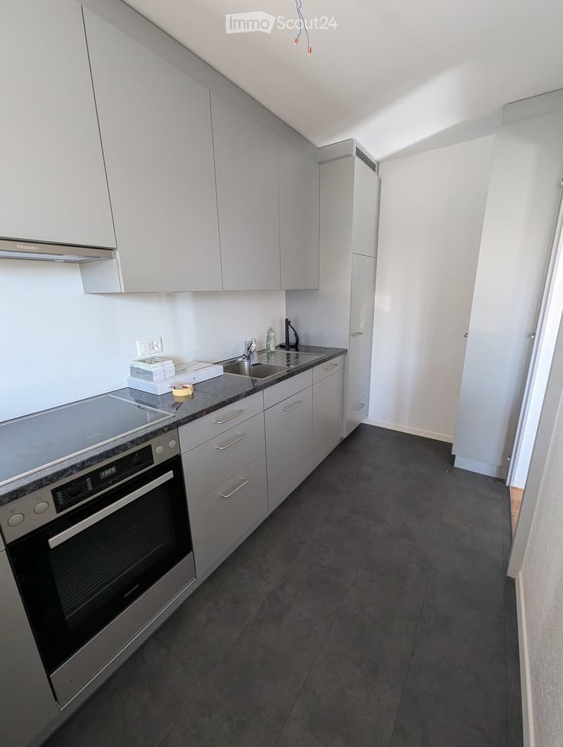 Modern kitchen with white cabinets, dark countertops, and stainless steel appliances including an oven and sink.
