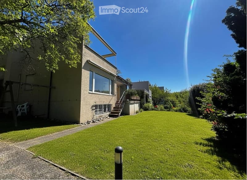 Modern house with a well-maintained garden, featuring a large lawn, a swing, and a pathway leading to the entrance.