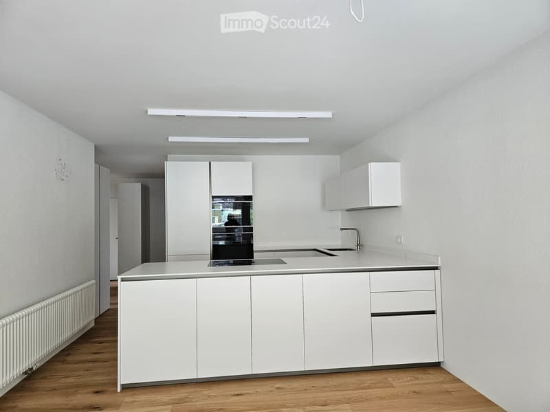 White cabinets, wooden floor, kitchen sink, electric stove, white ceiling, white walls, integrated lighting, white radiator.