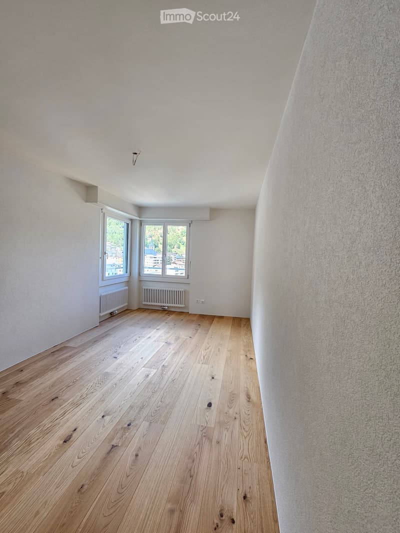 Spacious empty room with wooden floors and white walls, with windows and radiators, but no furniture or decor.