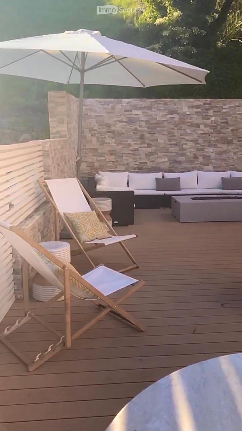 A wooden deck area with a sofa, fire pit, umbrella, and two wooden chairs.