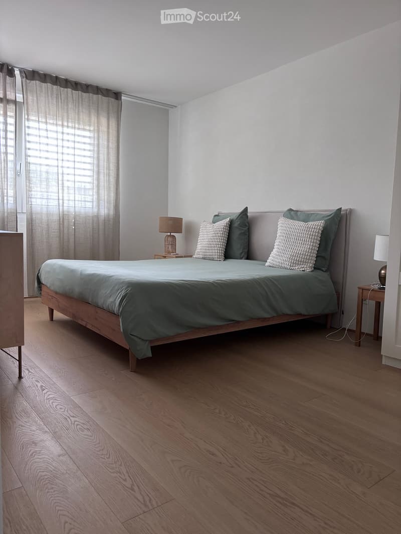 Modern bedroom with a wooden bed, green bedding, two nightstands with lamps, and a window with curtains.