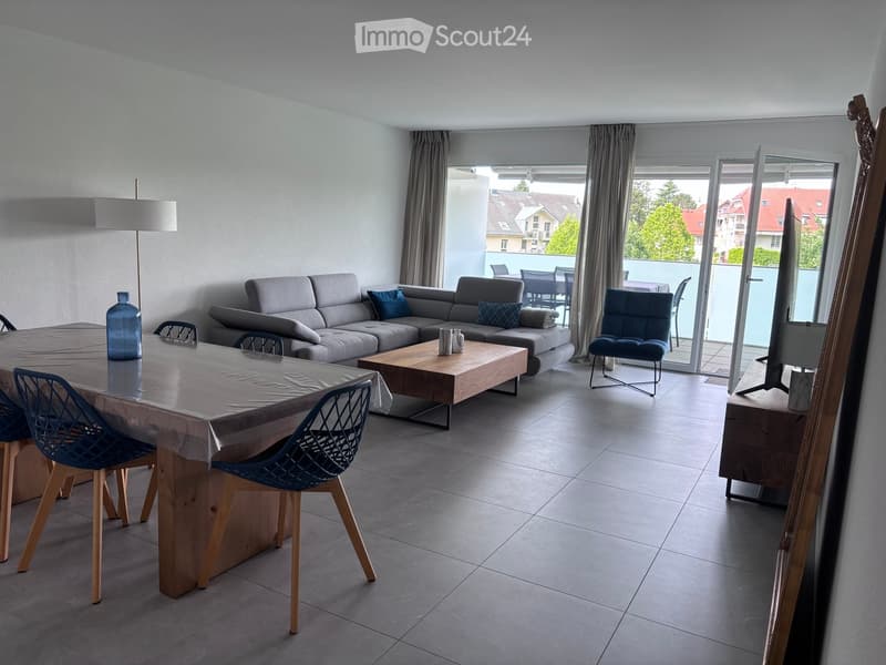 Modern living room with grey sofa, coffee table, dining table, chairs, and a view to a balcony.