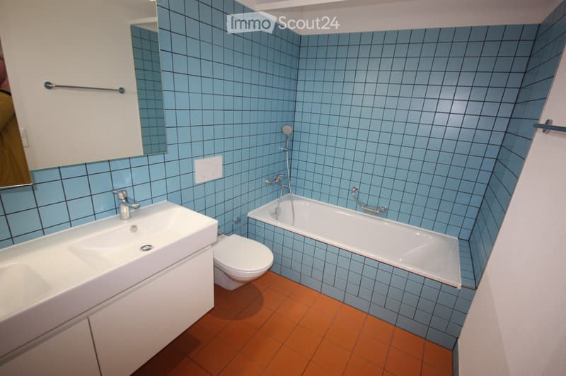 Modern bathroom with blue tiled walls, a white sink, toilet, bathtub, and a mirror above the sink.