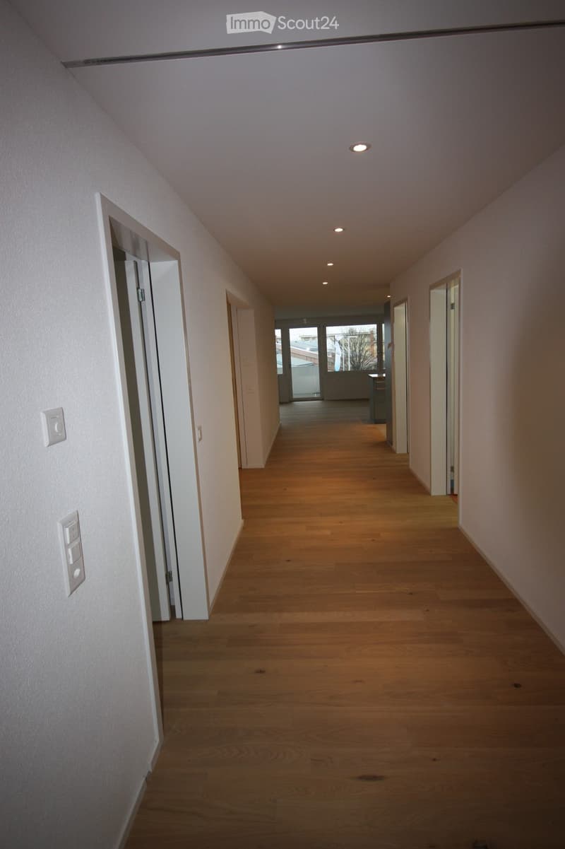 Empty hallway with wooden flooring, white walls, and recessed lighting. Doors are visible on both sides, leading to other rooms.