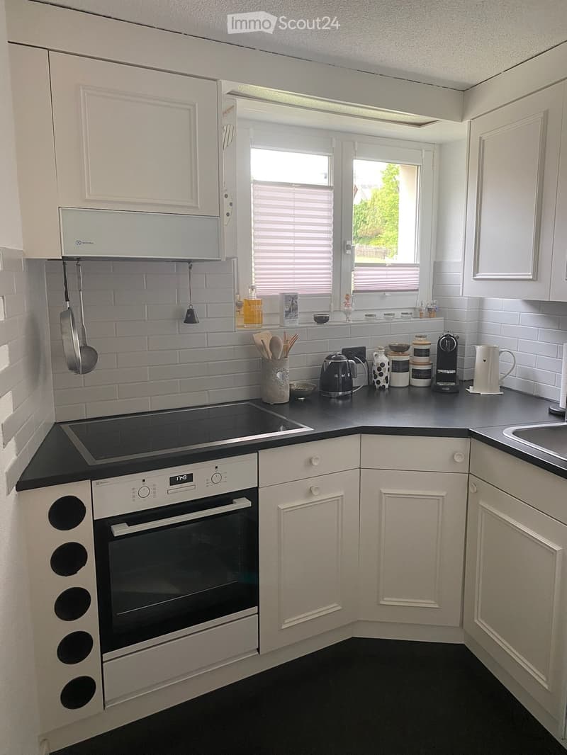 Modern kitchen with white cabinets, black countertops, and stainless steel appliances. Features an induction stove, oven, coffee maker, and various kitchen utensils on the counter.