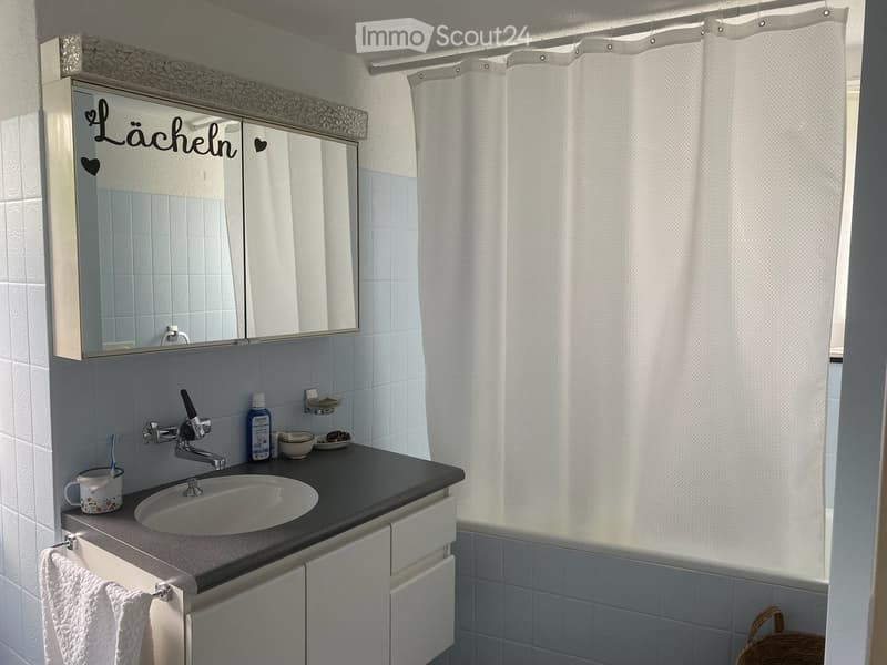 Bathroom with a sink, mirror, towel, and various toiletries on the counter. Shower curtain is visible in the background.