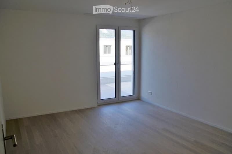 Empty room with wooden flooring, white walls, and a large sliding glass door leading to a balcony.