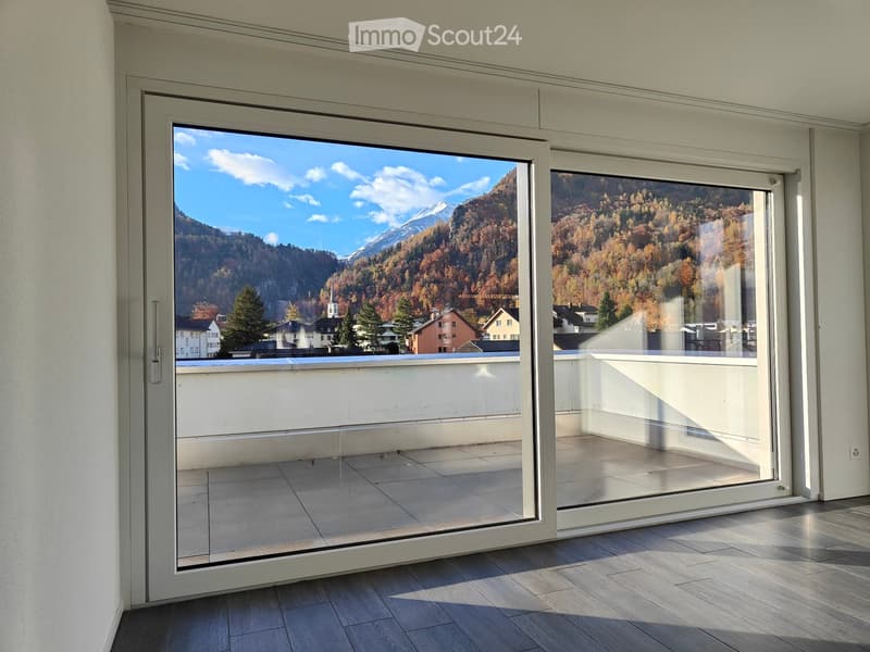 Large sliding glass doors open to a balcony with a scenic mountain view and autumn-colored trees.
