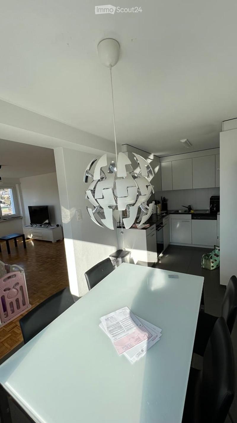 A modern, open-plan living and dining area with a sleek white dining table and chairs, a television in the living area, and a fully equipped kitchen with white cabinets, an oven, and a dishwasher.