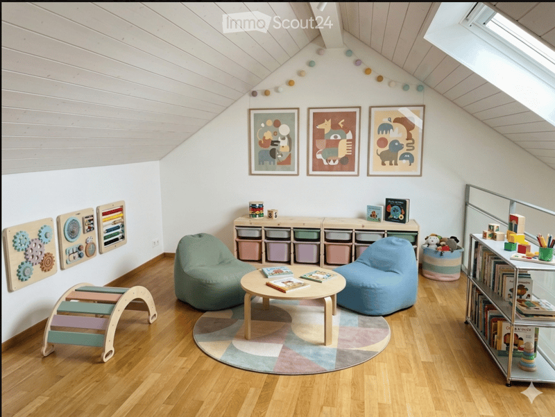 Bright, slanted-ceiling room with wooden flooring, two bean bag chairs, a small round table, a bookshelf, colorful storage bins, and decorative picture frames.