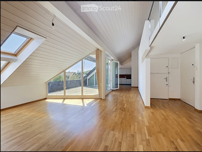 Bright, empty room with wooden flooring, white walls, and large windows, including a skylight and sliding glass doors leading to an outdoor area.