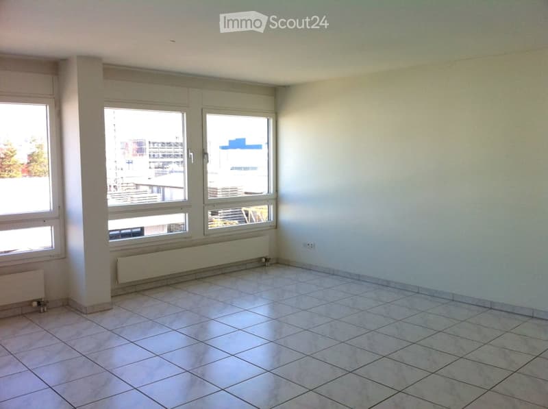 Empty room with tiled floor, white walls, large windows, and radiators along the walls.