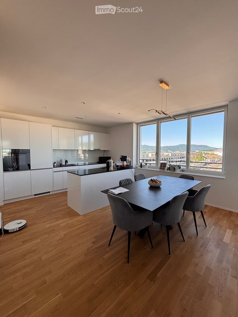 Modern kitchen and dining area with white cabinets, black countertops, a large dining table with six chairs, and a view of the cityscape through large windows.
