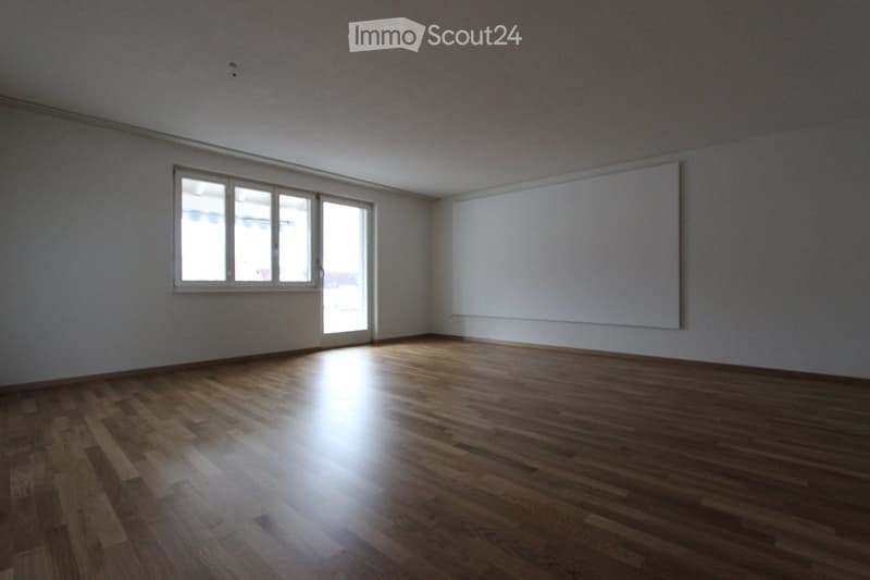 Empty room with wooden flooring, large window, and sliding glass door leading outside.
