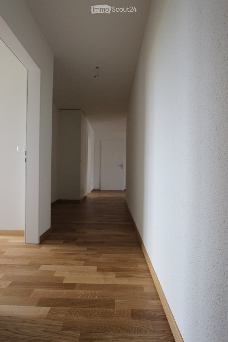 A narrow hallway with wooden flooring and white walls, featuring a closed door at the end.