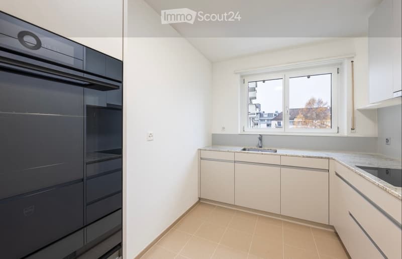 Modern kitchen with white cabinets, granite countertops, and a built-in oven. Features a window with a view of the city.