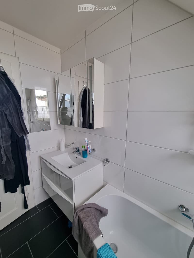 Modern bathroom with white tiles, a sink with a mirror cabinet, a bathtub, and a towel draped over the edge.