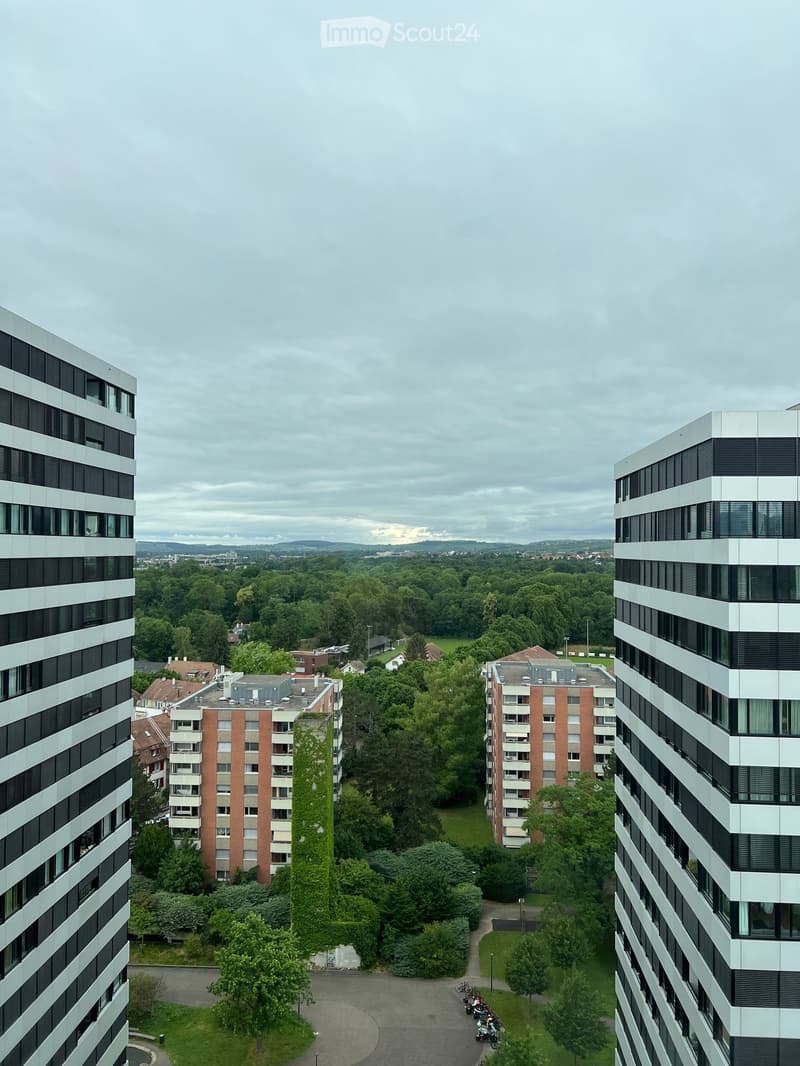 Aerial view of a modern residential complex with tall apartment buildings, greenery, and a parking area.