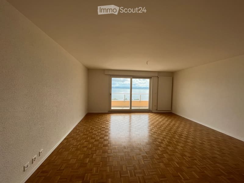 Empty room with wooden flooring, large window offering a sea view, and neutral-colored walls.