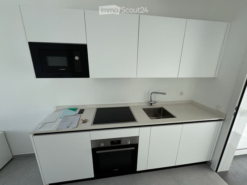 Modern kitchen with white cabinets, microwave, oven, induction cooktop, sink, and faucet.
