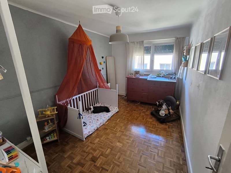Child's bedroom with a wooden floor, a small bed with a colorful canopy, a toy airplane on a shelf, a dresser with various toys, and a mirror on the wall.