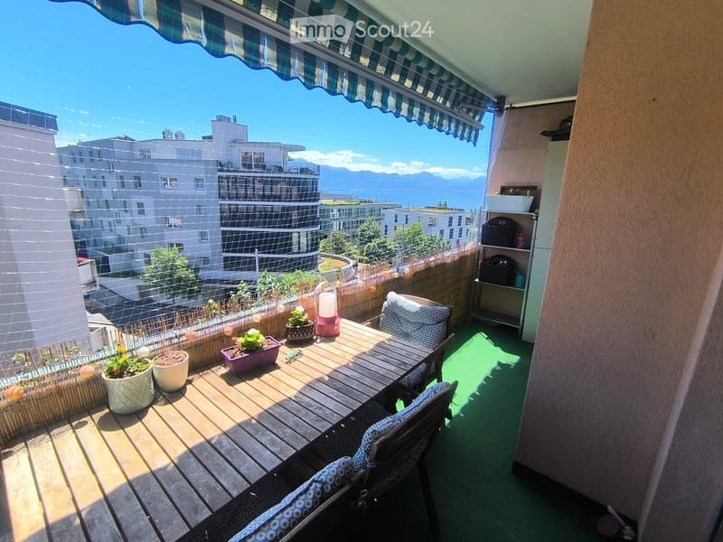 Balcony with wooden table, chairs, potted plants, and a scenic city view.
