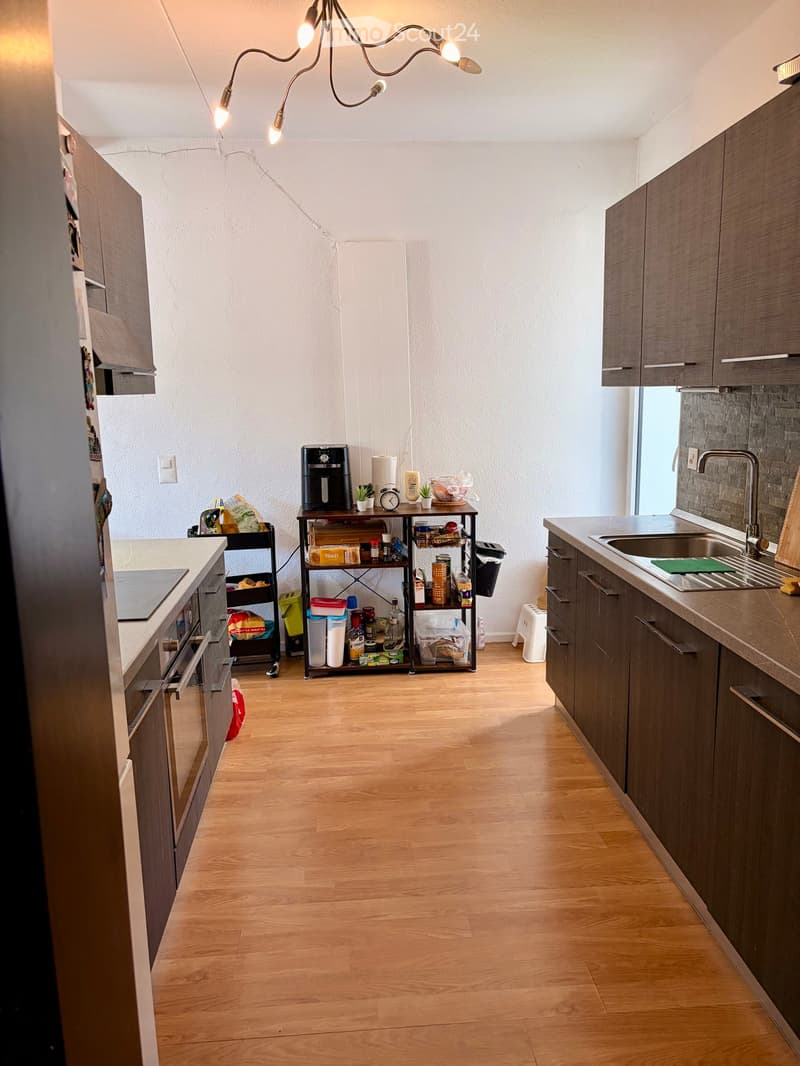 Modern kitchen with wooden flooring, grey cabinets, stainless steel sink, coffee maker, and various appliances.