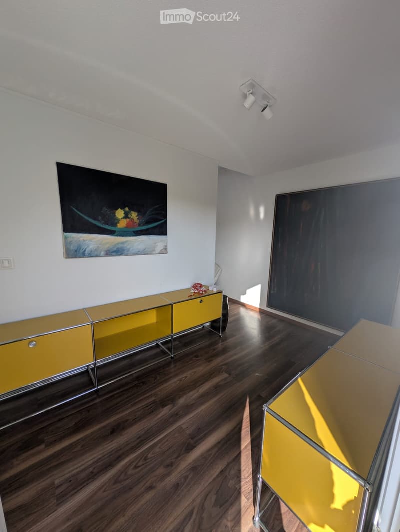 Modern living room with wooden flooring, yellow and glass cabinet, and a glass table.