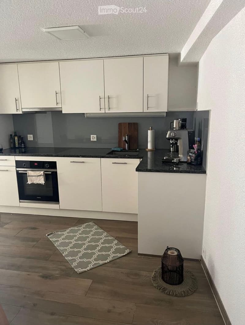 Modern kitchen with white cabinets, black countertops, wooden floor, and various appliances including an oven, coffee maker, and sink.