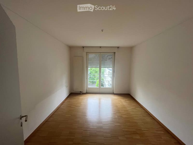 Empty hallway with wooden flooring, white walls, and a glass door leading to a balcony area.
