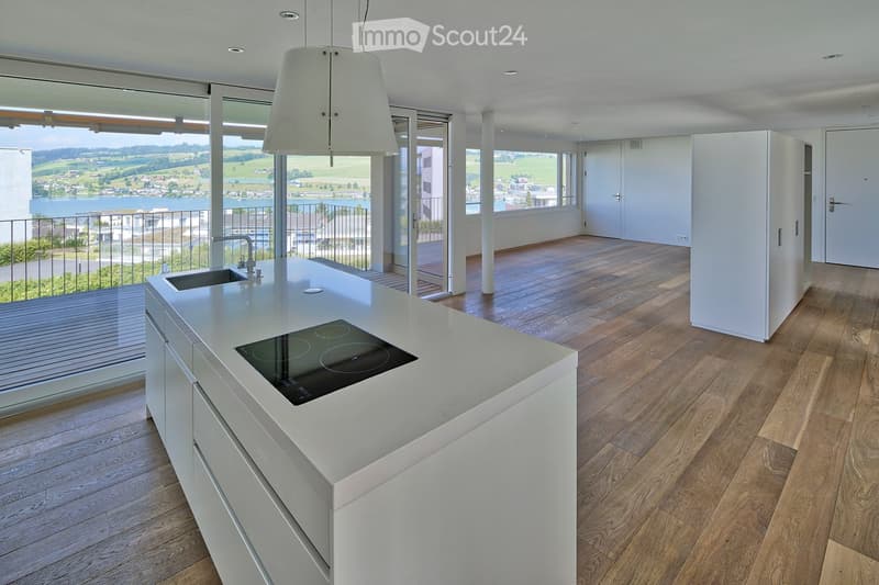 Modern kitchen with white island, induction cooktop, sink, pendant light, and large windows offering a scenic view.
