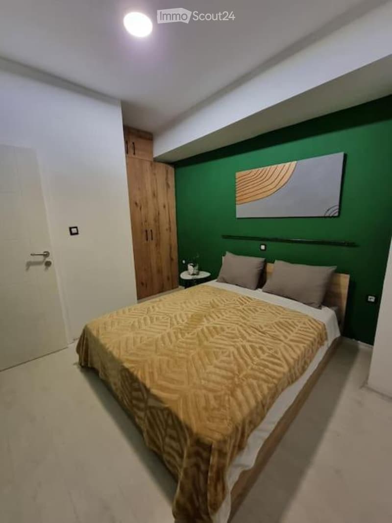 Modern bedroom with a large bed, nightstand, artwork on the wall, and a wooden wardrobe.