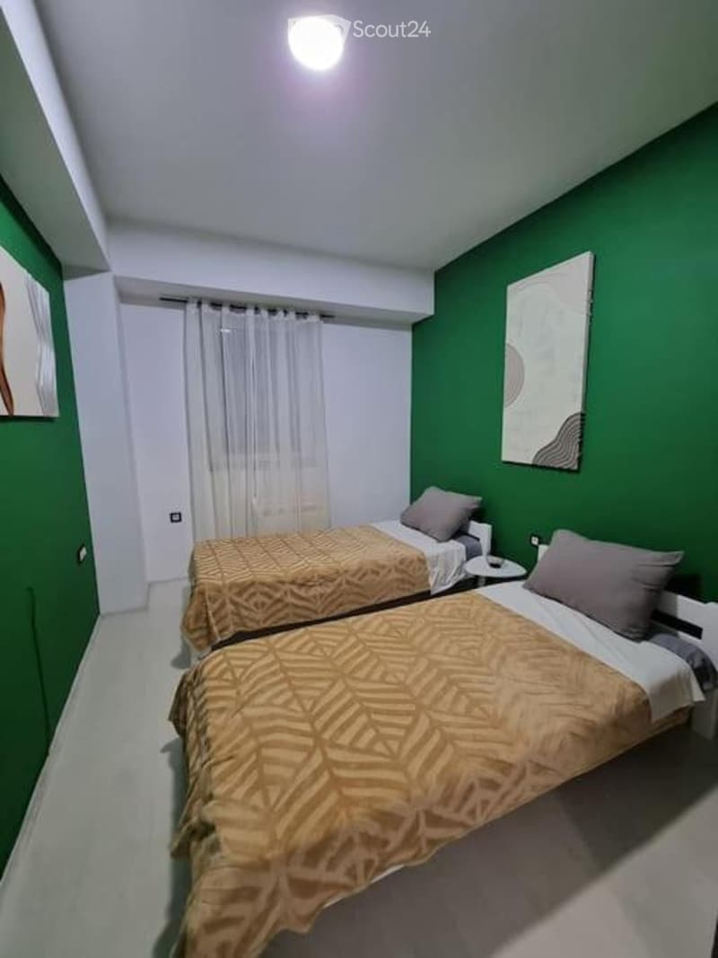 Cozy bedroom with two single beds, patterned bedspreads, nightstand, and modern artwork on green walls.