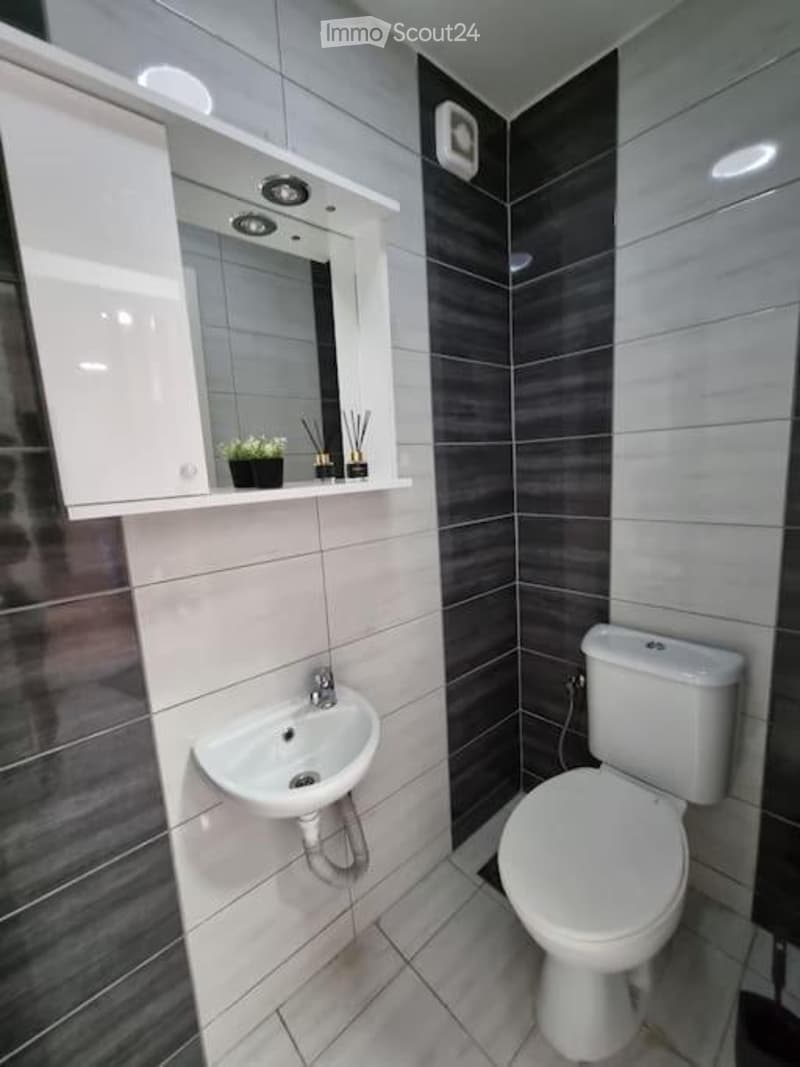 Modern bathroom with white tiles, dark grey accent wall, white sink, toilet, and mirrored cabinet.