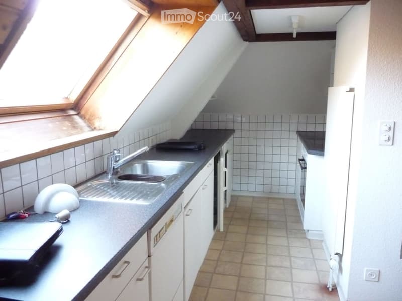 Compact kitchen with white cabinets, tiled walls, and a sink. Features a small window with wooden frame and a stove on the counter.