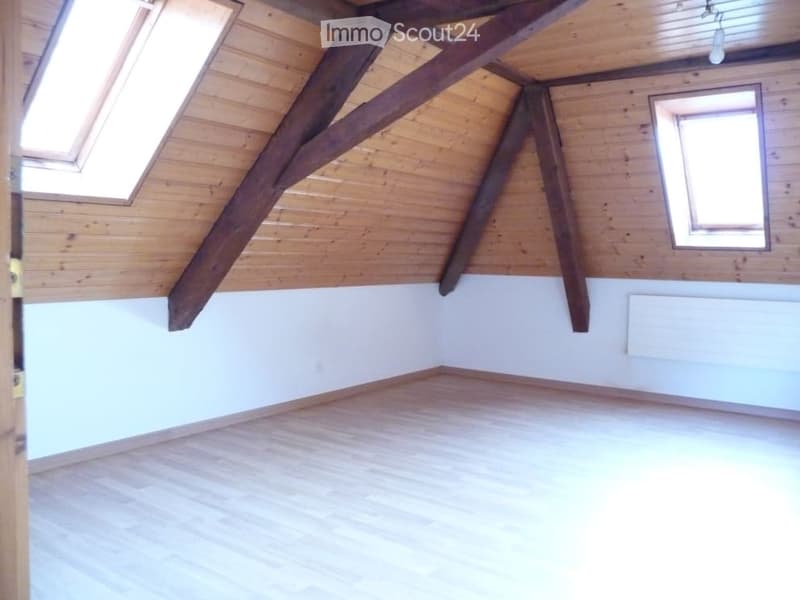 Empty attic room with wooden beams, wooden floor, and skylights. No furniture or equipment present.