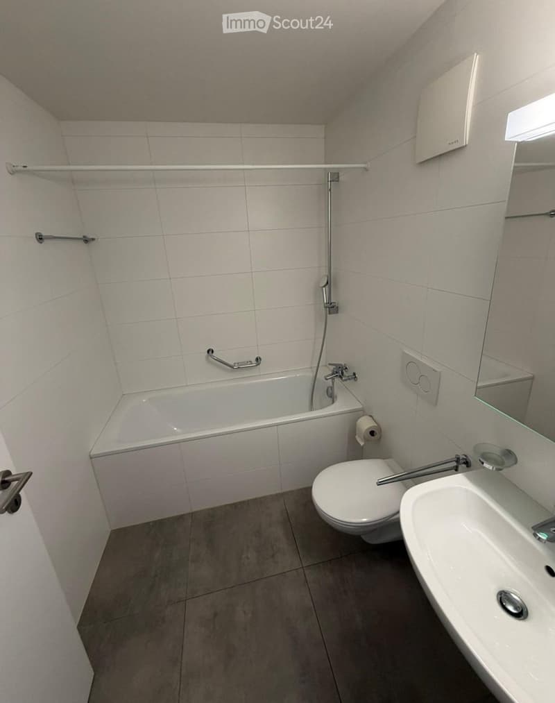 Modern bathroom with a bathtub, toilet, sink, and mirror. Features tiled walls and a grey tiled floor.