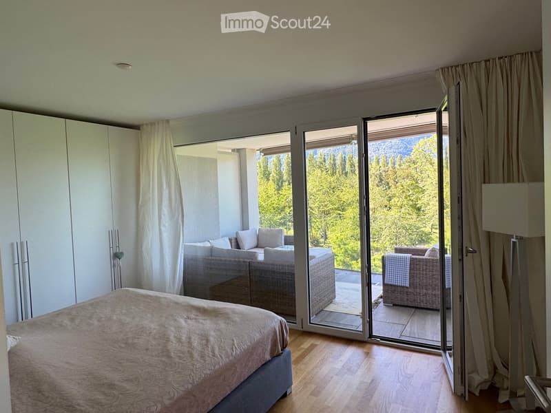 Modern bedroom with a large bed, sofa, and chair, leading to a balcony with scenic mountain views.