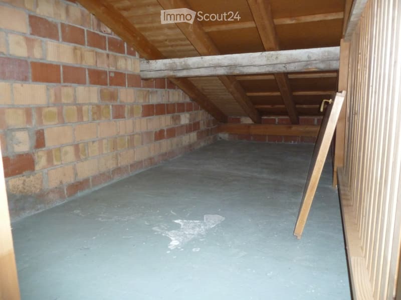 Empty attic space with exposed wooden beams, brick walls, and a concrete floor. No furniture or equipment present.