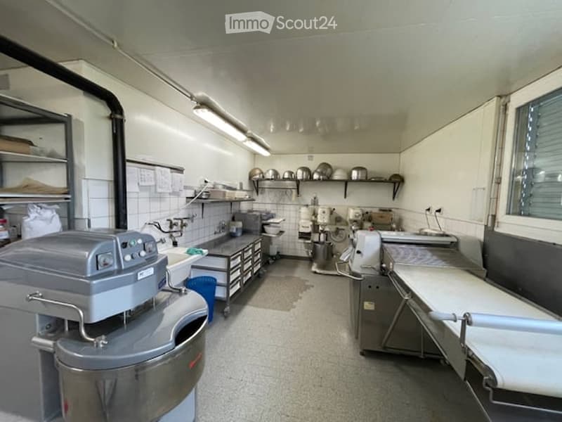 Commercial kitchen with stainless steel appliances, mixer, shelves, fridge, sink, and worktop.