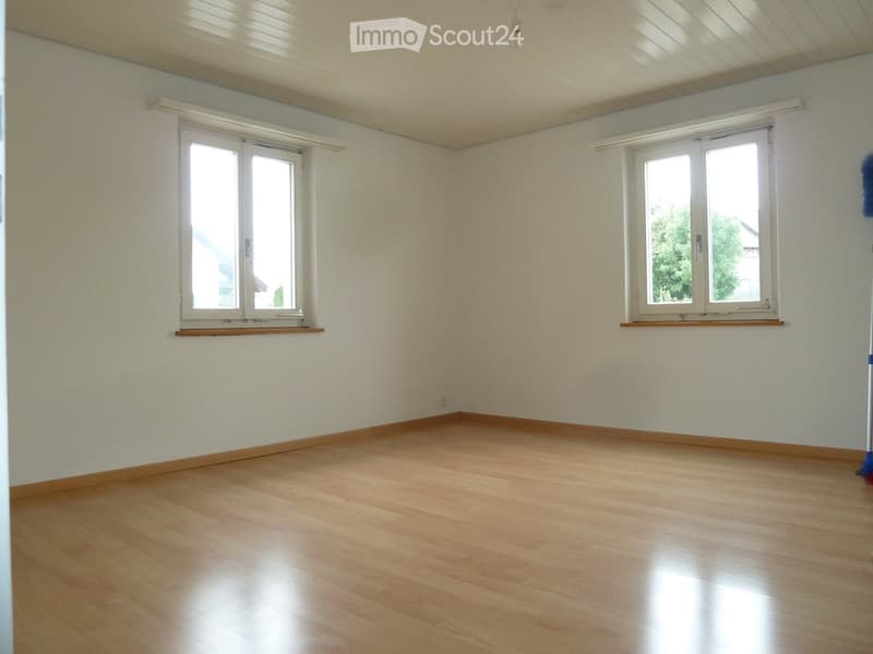 Empty room with light wooden flooring, white walls, and two windows with white frames and wooden sills.