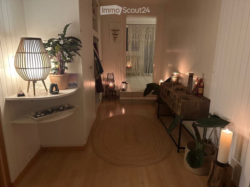 Cozy hallway with wooden flooring, a round woven rug, and various decorative items including plants, candles, and a wooden side table.