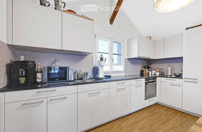 Modern kitchen with white cabinets, black countertop, coffee maker, microwave, oven, and various small appliances and items on the counter.