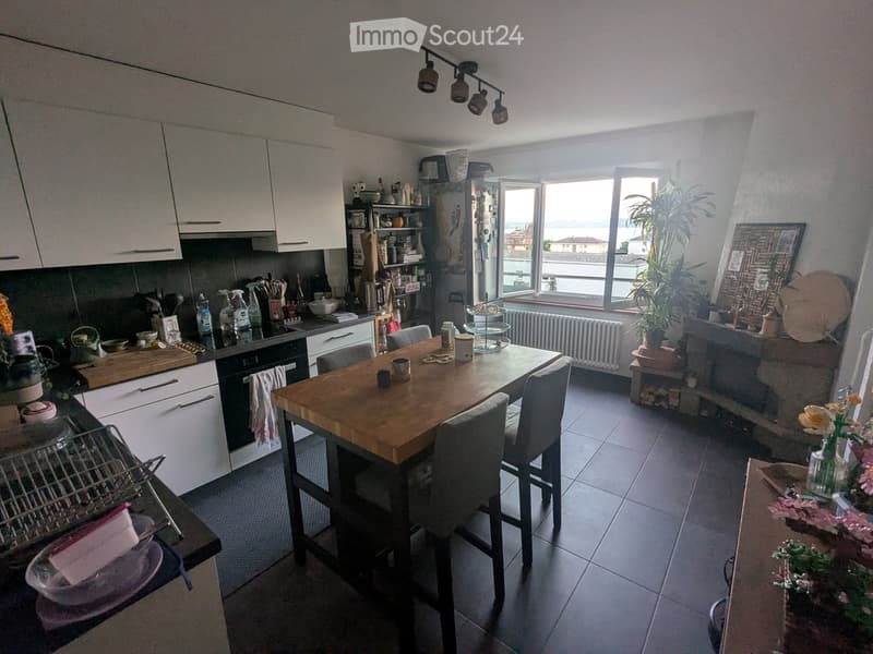 Modern kitchen with white cabinets, a wooden dining table with four chairs, and a view of the sea through large windows.